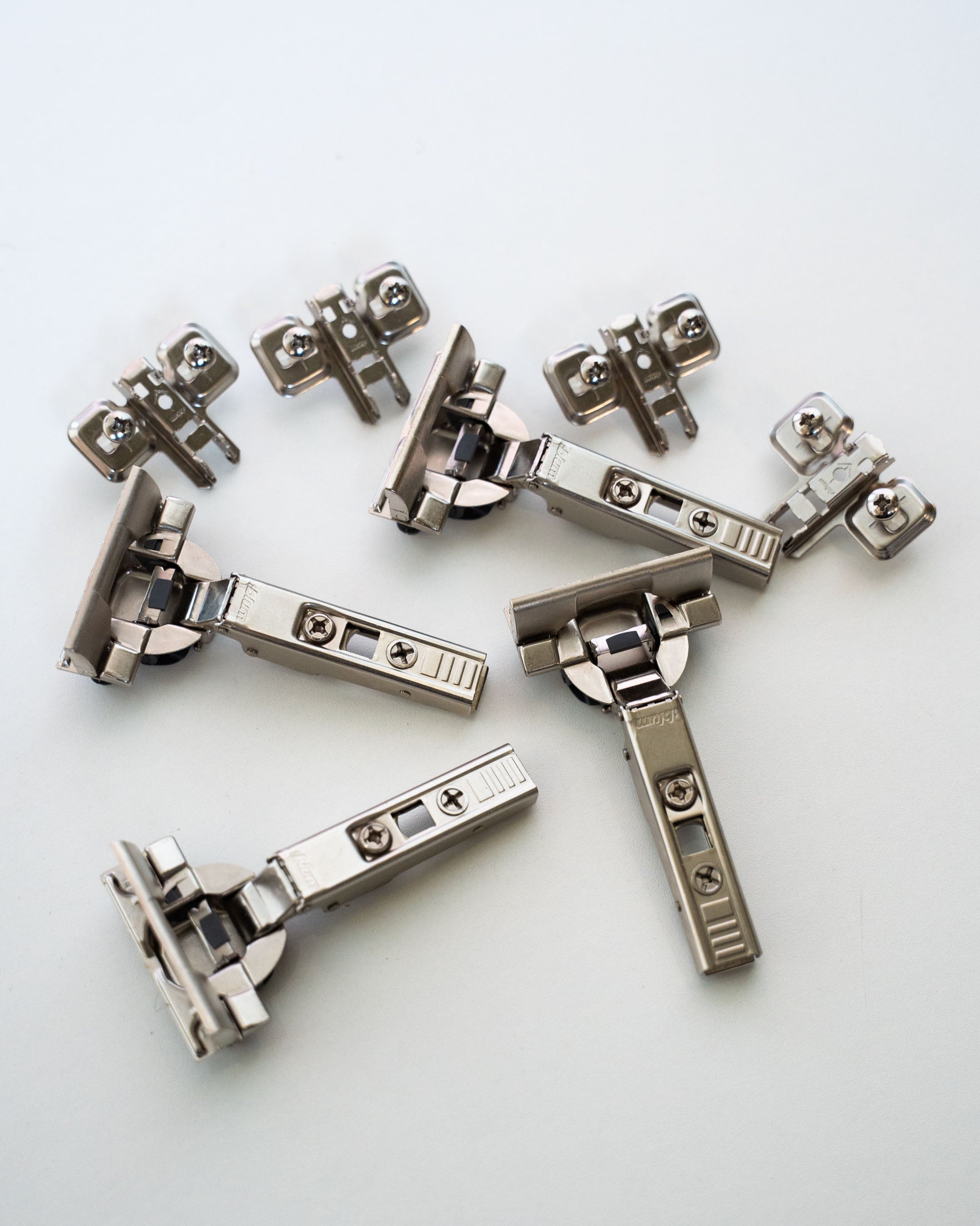 Ein Set aus mehreren Blum-Möbelscharnieren inklusive Montageplatten und Schrauben.