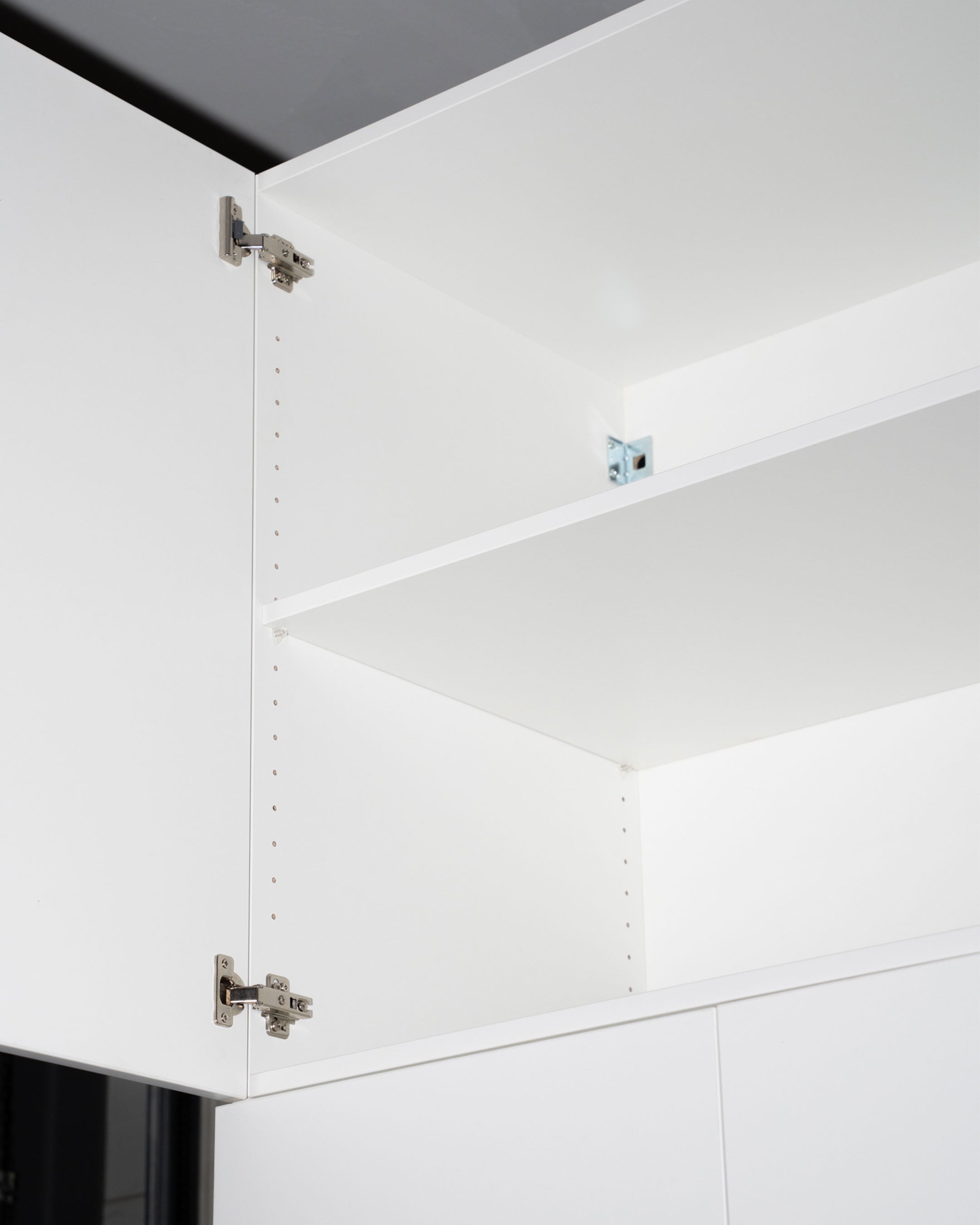 Ein weißer Einlegeboden in einem offenen Aufsatzschrank mit sichtbaren Scharnieren.