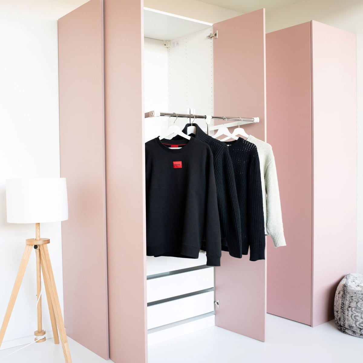 Ein weißer Kleiderlift für IKEA PAX Schränke mit hängender Kleidung in einem rosa Kleiderschrank.
