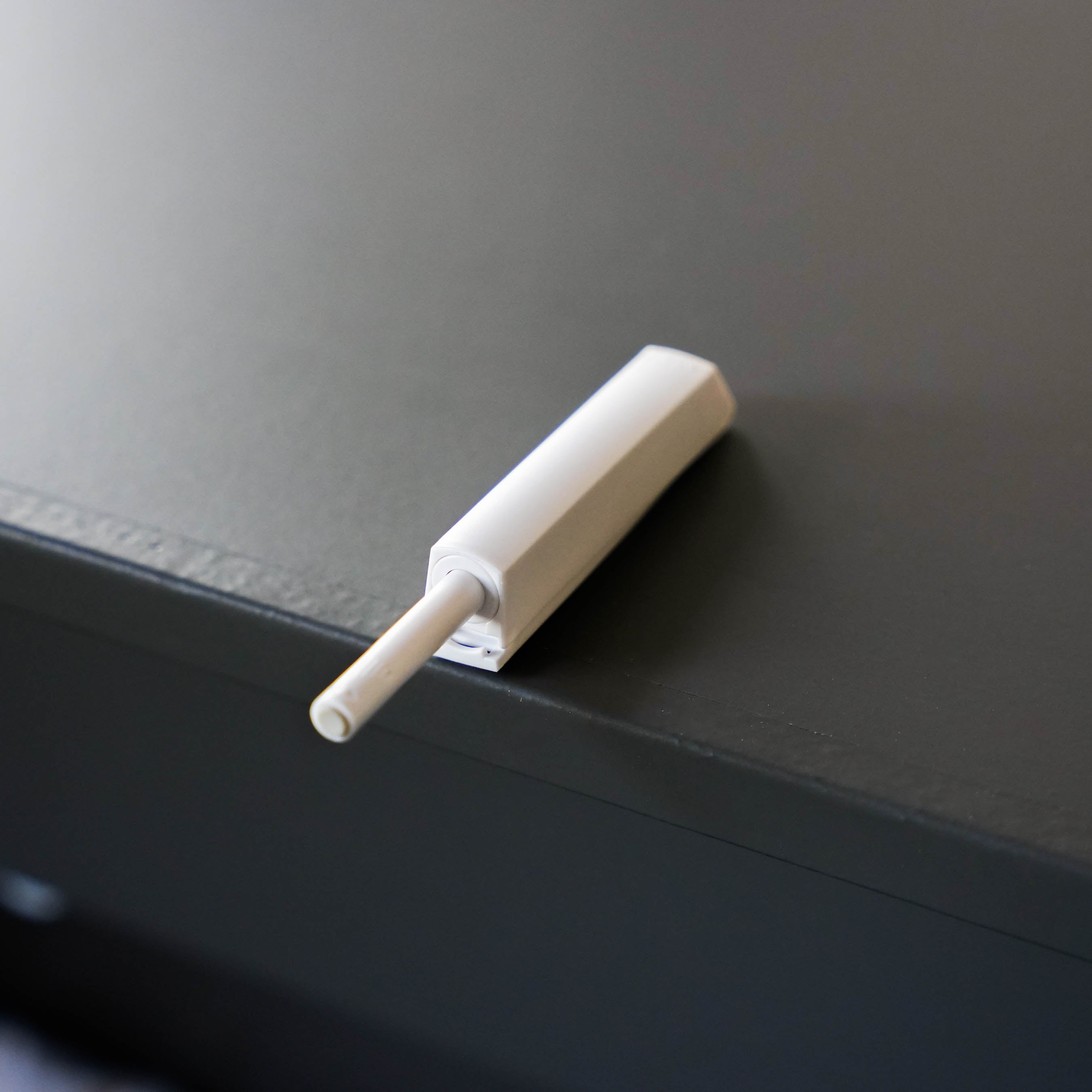 Ein weißer Tip-On-Drucktüröffner für grifflose Schranktüren auf einer dunklen Oberfläche.