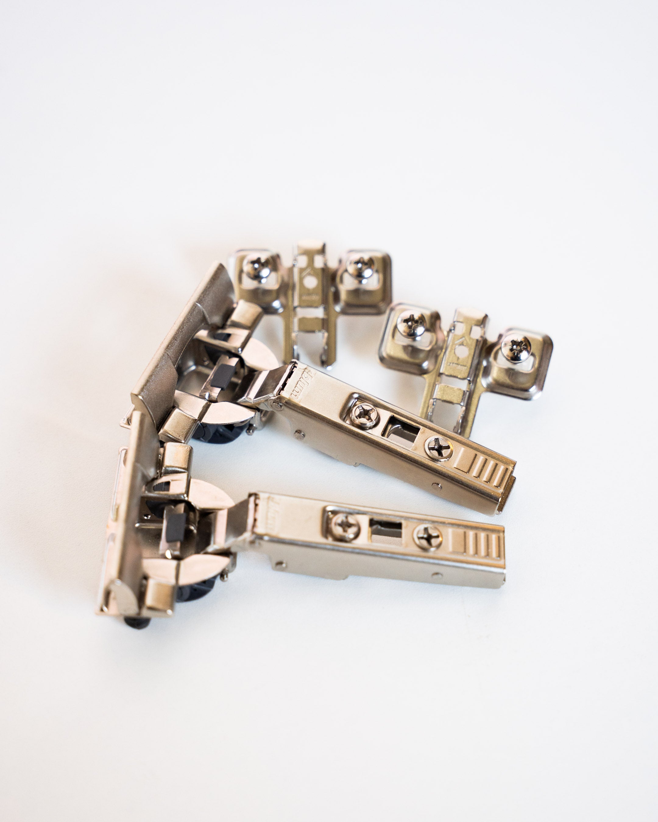 Ein Set aus zwei silberfarbenen Blum-Möbelscharnieren mit Montageplatten auf weißem Hintergrund.