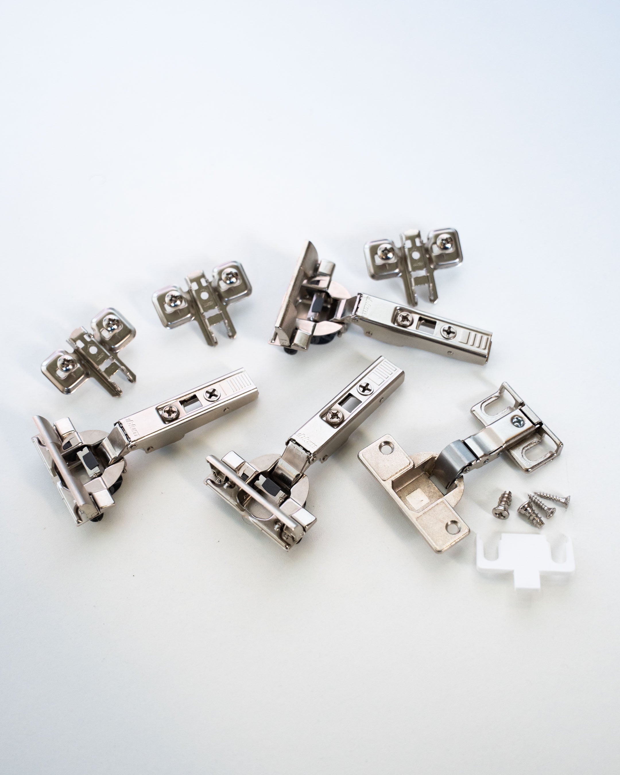 Ein Set aus Blum-Scharnieren mit Montageplatten, Schrauben und einer weißen Abdeckung.