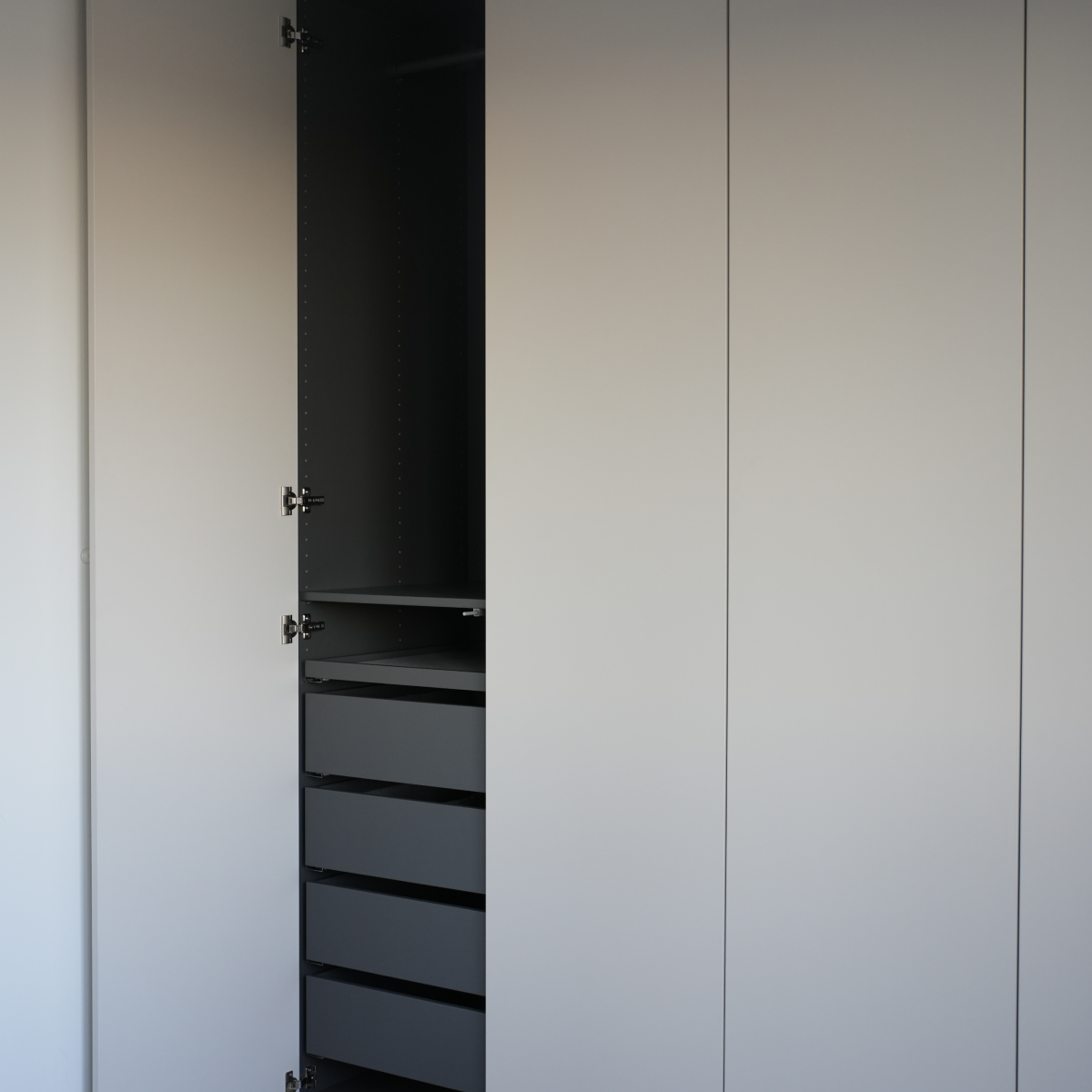 Ein moderner, griffloser Kleiderschrank mit einer offenen Tür, die Einlegeböden und Schubladen zeigt.