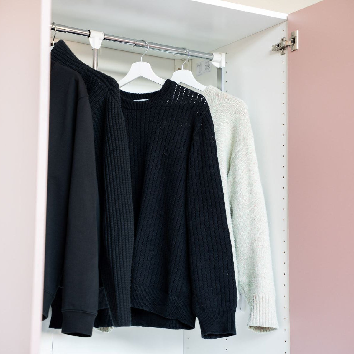 Ein Kleiderlift für IKEA PAX Schränke mit drei hängenden Pullovern an einer Kleiderstange.