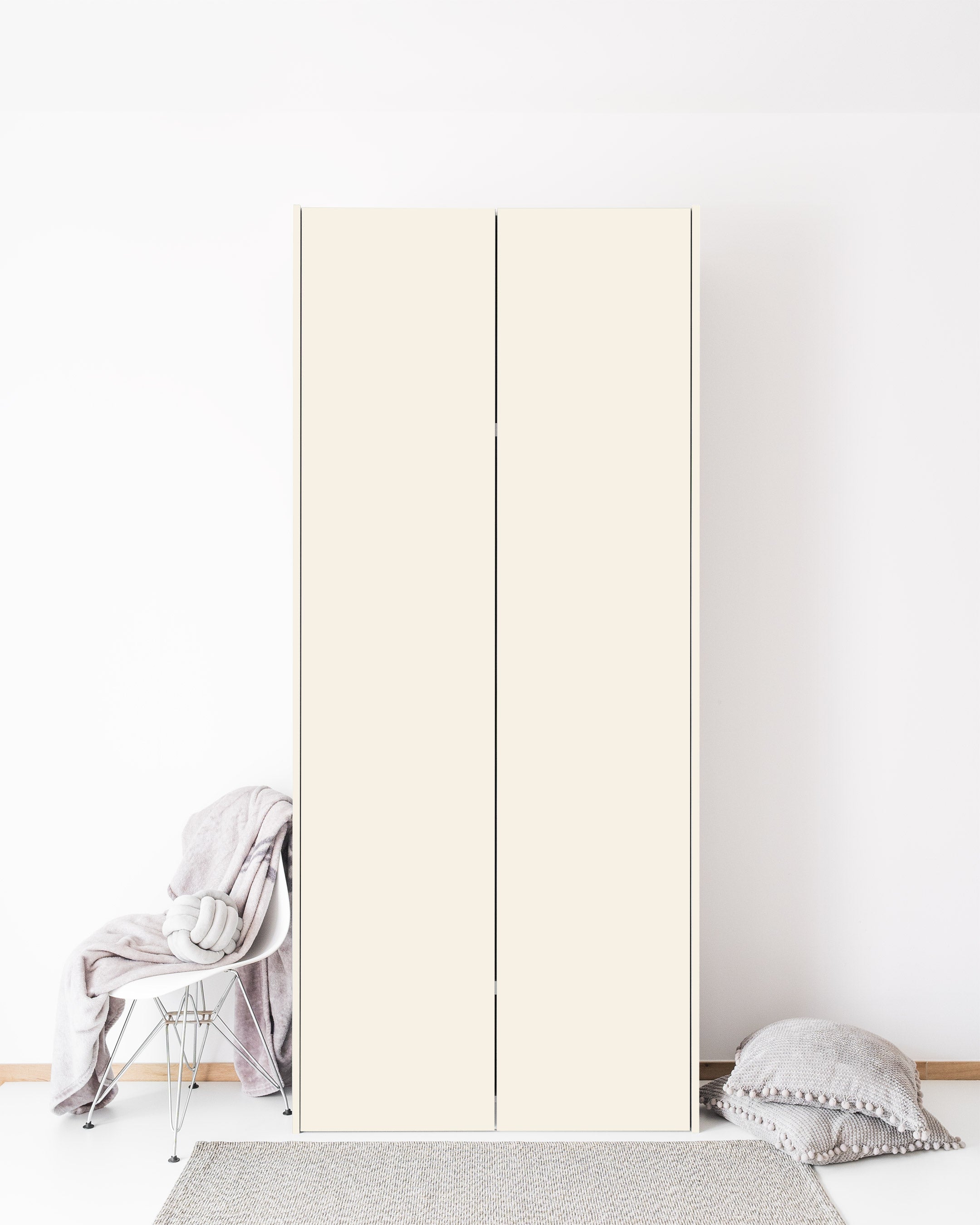 A tall, minimalist wardrobe with two smooth, cream-colored doors stands against a white wall.