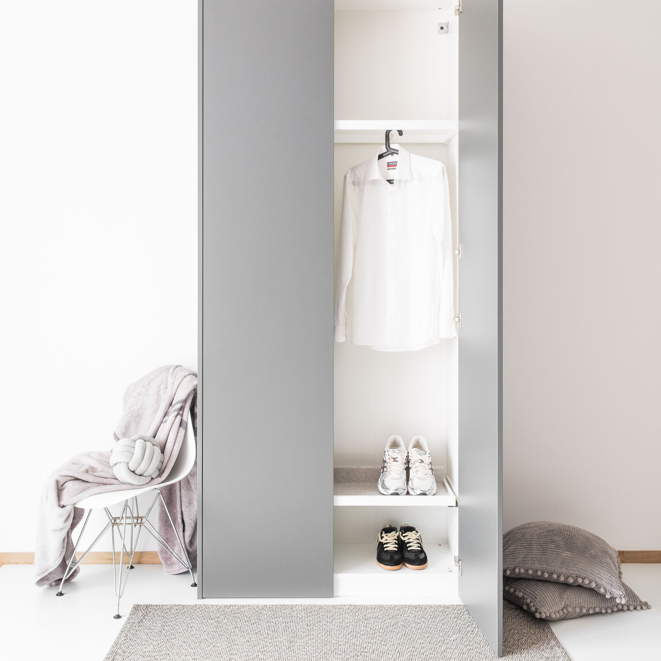 Ein grauer PAX Kleiderschrank mit einer offenen Tür, in dem ein weißes Hemd und zwei Paar Schuhe stehen.